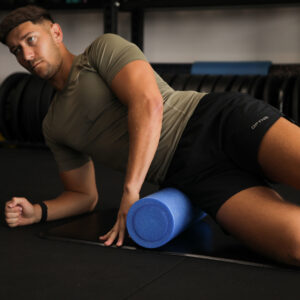Fitness Mad 45cm high density blue foam roller being used by a man for IT band and leg muscle recovery in the gym