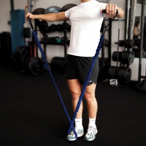 A man in a gym doing a lateral raise with a blue resistance trainer
