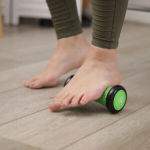 Woman using a green and black coloured foot massage roller for plantar fasciitis