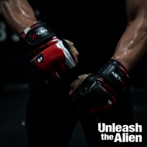MET-X Alien Force MMA gloves on fighter's hands in dark gym – red and black alien design with 'Unleash the Alien' text
