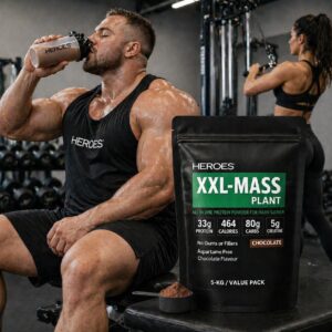 Bright gym scene featuring Heroes XXL-MASS Plant Chocolate 5kg protein powder bag in the foreground, with a large muscular man drinking a chocolate protein shake and a fit woman training in the background.