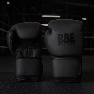 BBE UNIFY4 Matte Black Leather Boxing Gloves displayed in a hardcore boxing gym with ring and punching bags – premium wrist support, high-density padding, and durable leather for elite training and sparring.